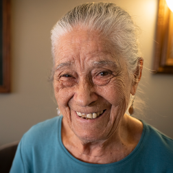 Vicenta, a homebound older Citymeals on Wheels recipient with white hair smiles in her apartment.