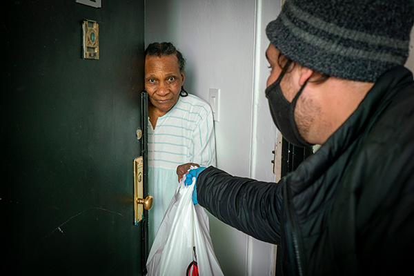 Volunteer delivers a meal to an older African-American woman in NYC