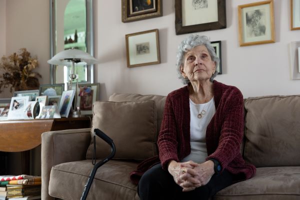 Helen, an older woman, sits on the couch, looking off into the distance.. 