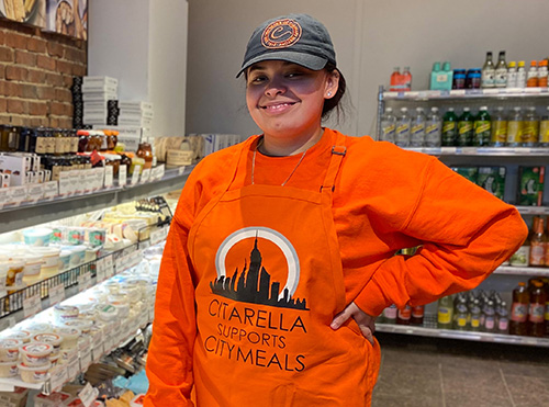 Citarella employee in an orange apron that says "Citarella supports Citymeals"