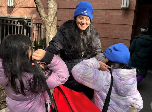 Several students and an adult chaperone carry meal delivery bags outside of an apartment building.