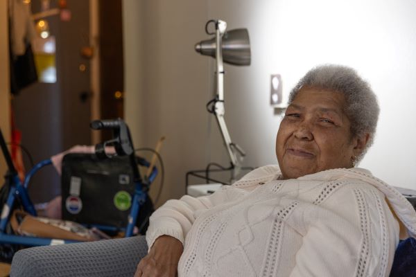 An older woman sitting on the couch, a walker visible in the background.