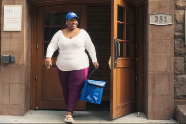 Letisha wears a Citymeals hat and carrys a Citymeals delivery bag.