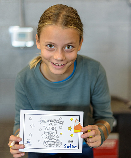 A young Citymeals volunteer holds up a handmade Halloween card. 