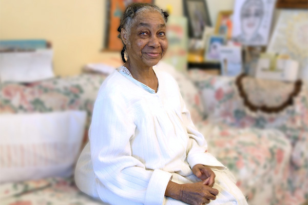 Thelma, a Citymeals on Wheels recipient, is a senior woman in a white nightgown in her New York City apartment. 