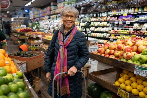 An older woman, Rebecca, stands in the middle of a grocery store.