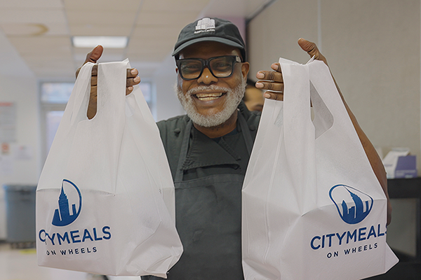Chef holding up bags with the Citymeals on Wheels Logo