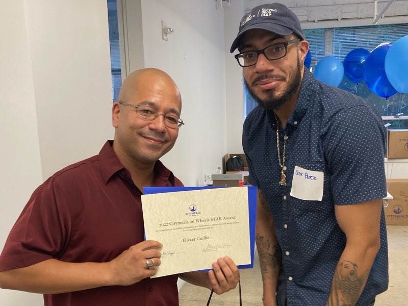 Volunteer Eli (left) holds his award standing next to Citymeals staff member Cesar