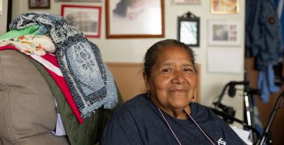 Anita, an Hispanic woman, sits in an armchair in the living room of her apartment.